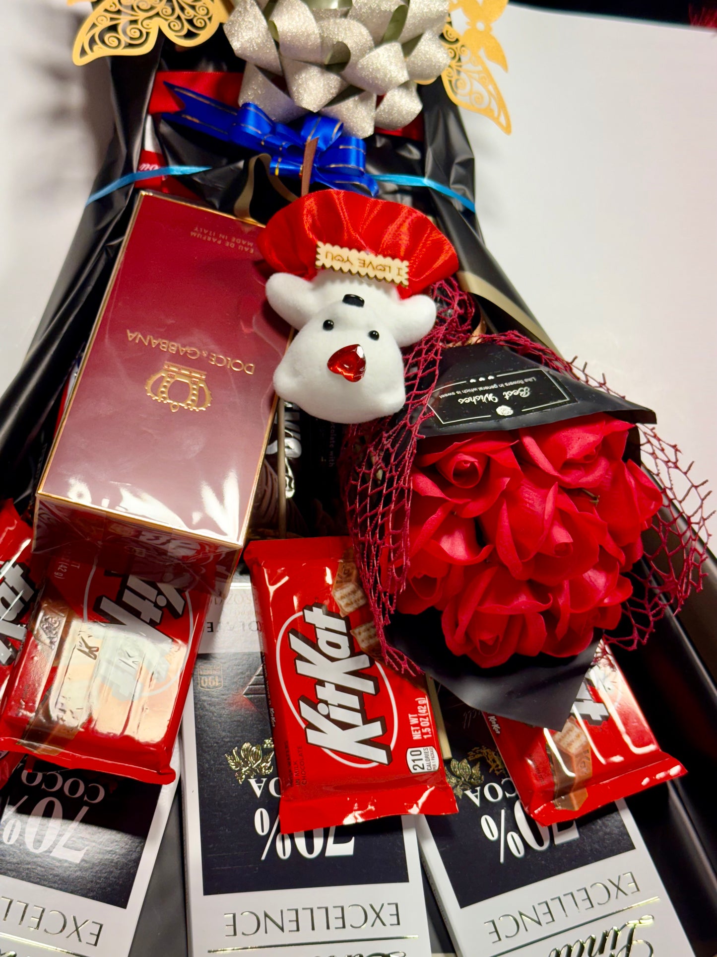 Assorted chocolate bars including KitKat and Lindt, with a decorative bear figurine and red flowers.