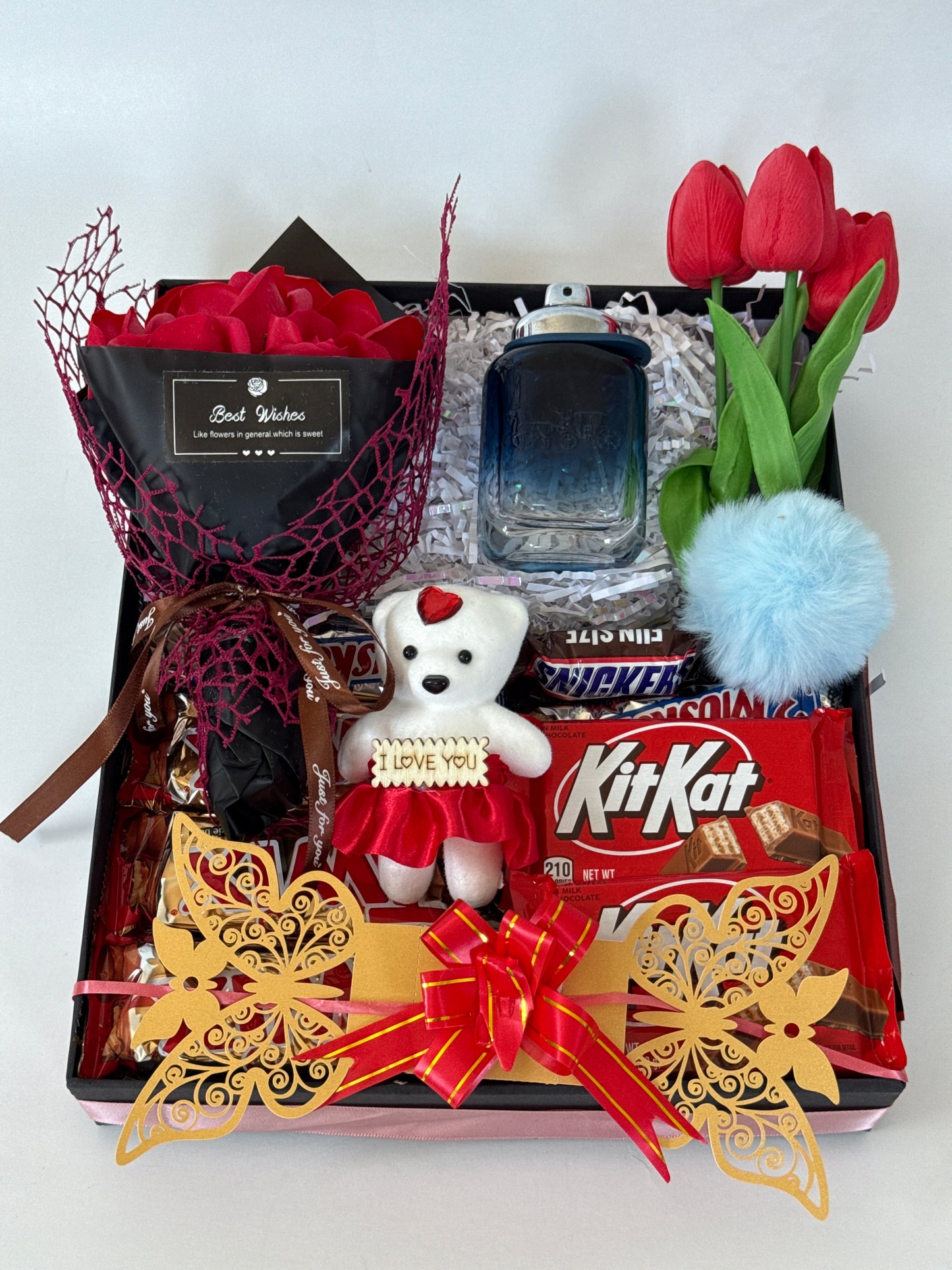 Gift box with various items including KitKat bars, a small teddy bear, and decorative elements on a white background.