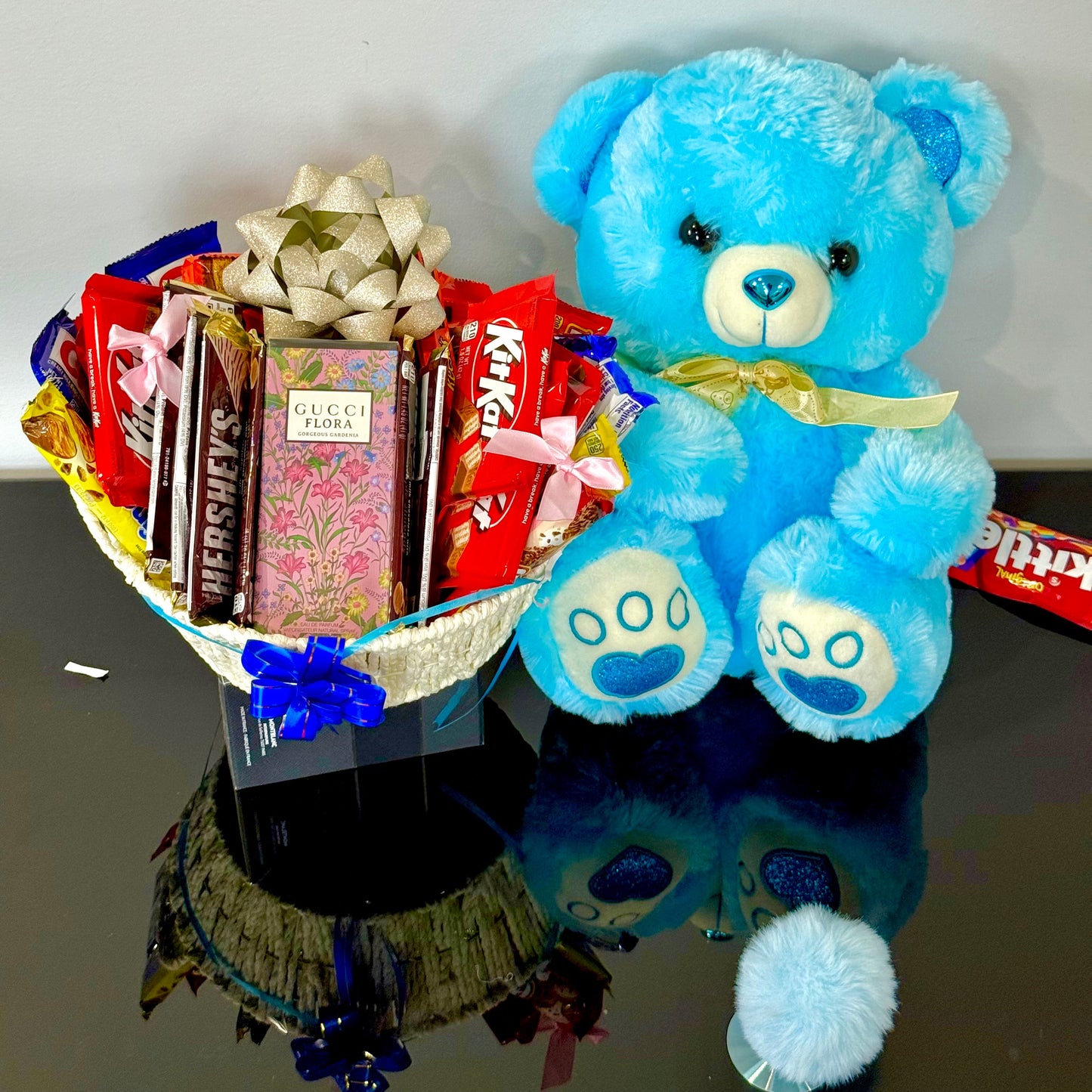 Blue teddy bear with a basket of chocolates on a reflective surface