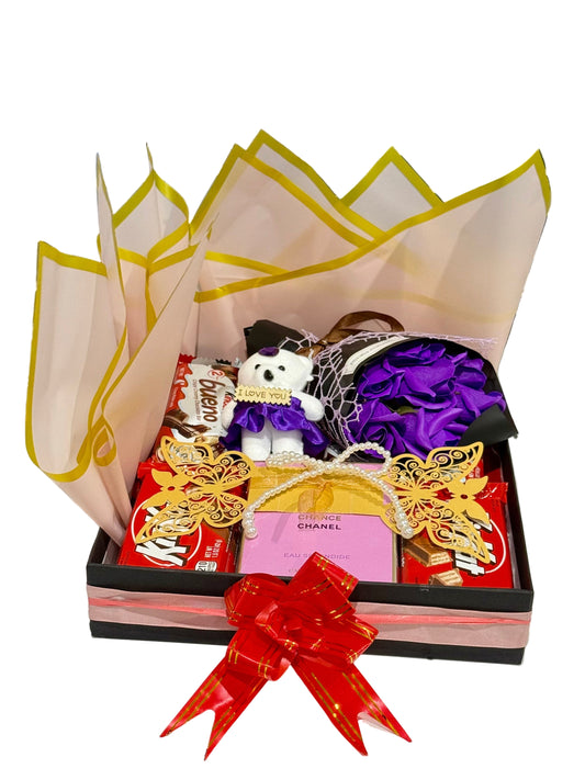 Gift box with decorative items including a bow, small figurine, and purple flower arrangement on a window sill.