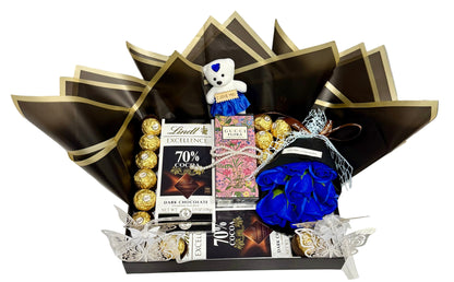 Gift basket with chocolates, candies, and a teddy bear on a table.