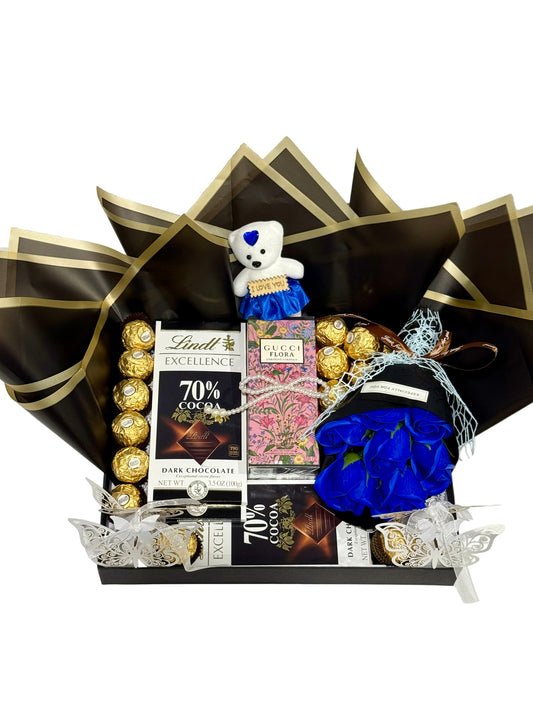 Gourmet gift basket with chocolates, Lindt Excellence chocolate bars, and a teddy bear on a white surface.