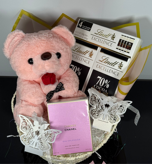 Pink teddy bear, Chanel perfume, and Lindt chocolate bars on a decorative stand.