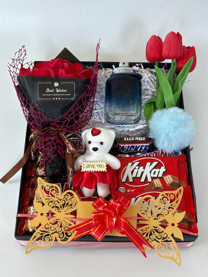 Gift box with various items including KitKat bars, a small teddy bear, and decorative elements on a white background.