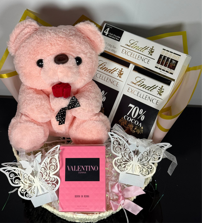 Pink teddy bear with Lindt chocolate bars and Valentino perfume on a decorative background