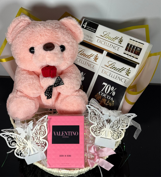 Pink teddy bear with Lindt chocolate bars and Valentino perfume on a decorative background