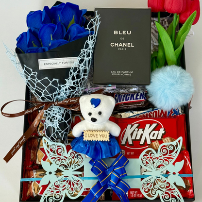 Gift basket with blue roses, teddy bear, KitKat bars, and Chanel perfume on a white background
