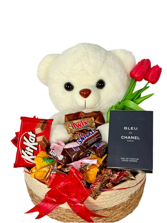 Gift basket with teddy bear, chocolates, flowers, and perfume on a white background